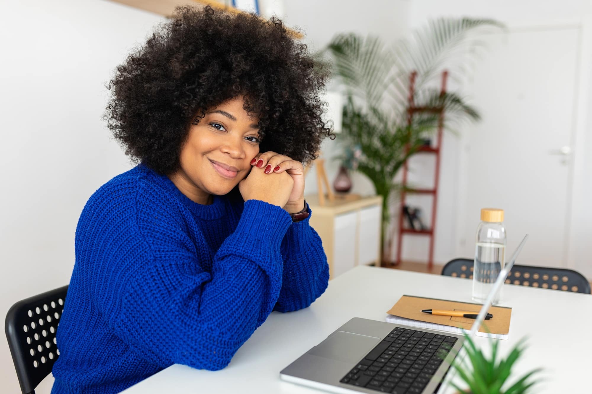 Portrait of young black woman with laptop looking at camera sitting at table